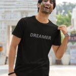 A man and woman wearing couple t-shirts. The man's shirt says "Dreamer" in Hinglish with a creative design. The woman's shirt says "Visionary" in Hinglish with a complementary design.